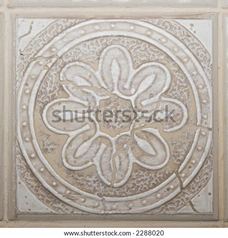 Color DSLR picture of square off white, tan or beige decorative ceramic tile with flower pattern and relief texture.