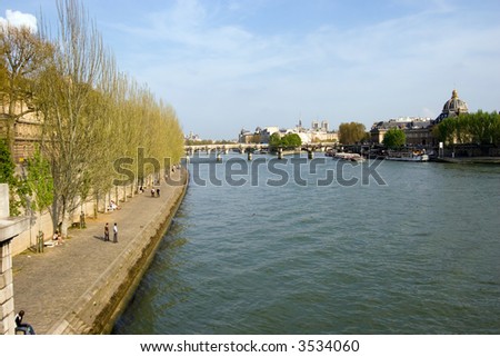 Looking up the Seine River, with houses and buildings lining the river and clouds in the background