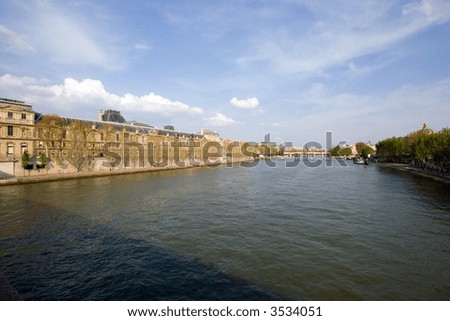 Looking up the Seine River, with houses and buildings lining the river and interesting clouds in the background
