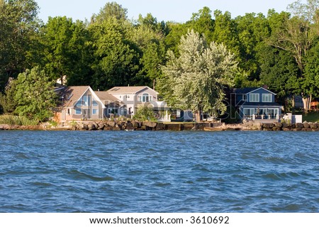 Wide view of a lake house on Ontario Lake, with water in the foreground and trees in the background