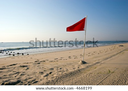 Color DSLR picture of a red warning flag on a sand beach, New Jersey Shore.  Atlantic Ocean is calm in background but signal warns of potential danger. Horizontal orientation with copy space for text.