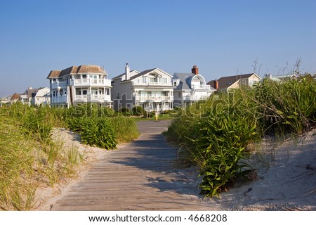 Color DSLR picture of luxury vacation beach houses along the New Jersey shore, with grass covered sand dunes in the foreground and clear blue sky background. Horizontal with copy space for text.