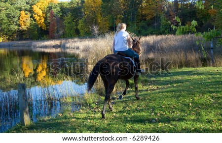 Color DSLR image of young girl riding a brown horse by the still pond.  Green grass and forest in background.  Horizontal orientation with copy space for text.
