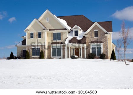 Color DSLR image of contemporary luxury colonial suburban house on hill. Home has snow in the foreground and a bright, clear blue sky background. Horizontal with copy space for text.