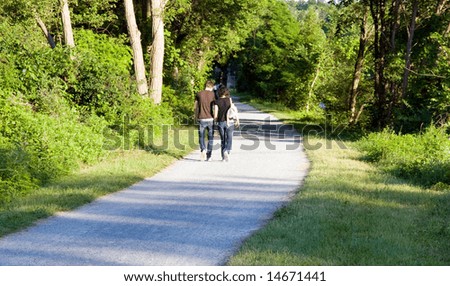 Color DSLR image of loving couple (male and female) walking along a path through the woods.  Boy and girl are facing away, strolling along wooded path. Horizontal with copy space for text.