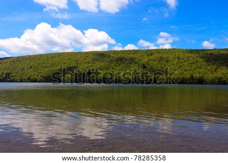 Color DSLR landscape picture of Canadice Lake, one of New York Finger Lakes in late spring.  The calm water is clear, the hills green and the sky a bright blue. Horizontal with copy space for text.