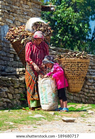 ANNAPURNA AREA, NEPAL - MARCH 26: Nepalese woman and daughter with baskets on the road on March 26, 2014 in Annapurna District, Nepal.