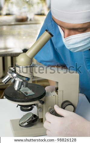 a doctor or scientist as he studies something through a microscope.