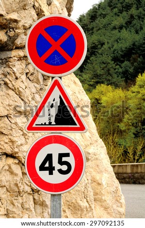 Three  traffic signs: speed limit sign, no stopping sign and the sign warning about rockfall. France.