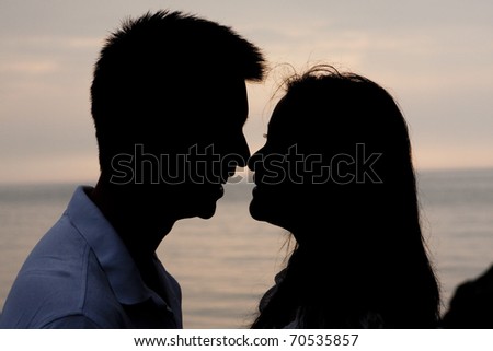 Silhouette of a young couple with their faces close against dawn on the lake