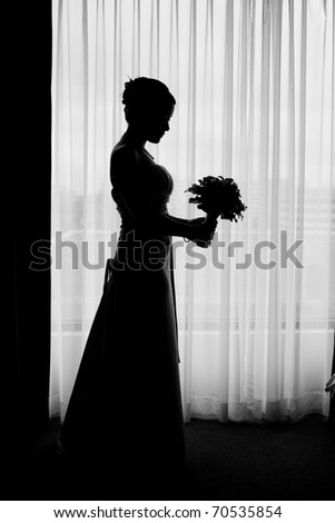 Silhouette of bride besides the window with her wedding bouquet