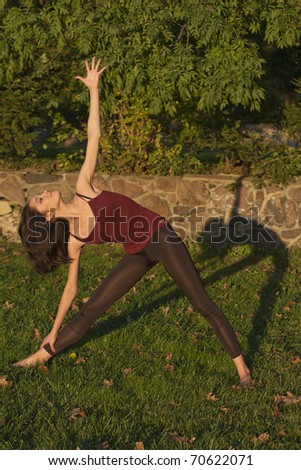 Triangle posture (trikona-asana): Young sporty slim woman doing yoga on the open air during warm autumn day