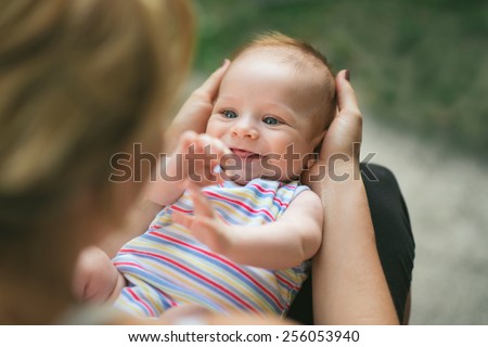 Portrait of a beautiful, laughing baby boy with gorgeous blue eyes being held by his mother, on his back, in her lap in the garden
