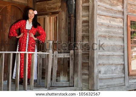 Traditional folklore woman saying welcome in Bulgaria in front of her wooden house