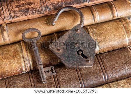 Open padlock and rusty key lying on ancient books