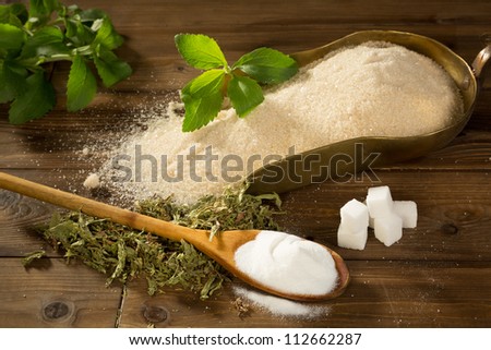 Crystal sugar and lumps together with powder and dried stevia natural sweetener on a wooden table