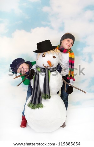 Two happy sisters playing around their snowman