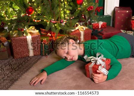 Young girl sleeping in front of the christmas tree holding her gift