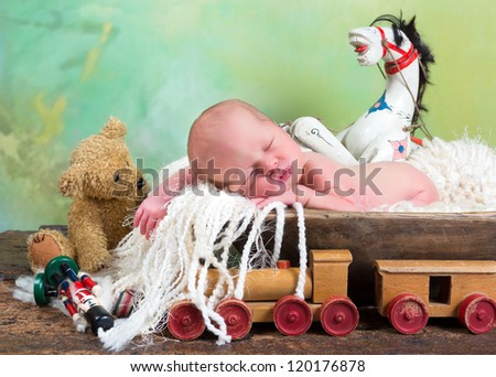Newborn baby sleeping in a trench bowl surrounded by vintage antique toys