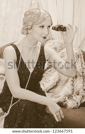 Old photo with reenacted scene of a classy lady in roaring twenties style using a pair of opera glasses - grain has been added for vintage photo look
