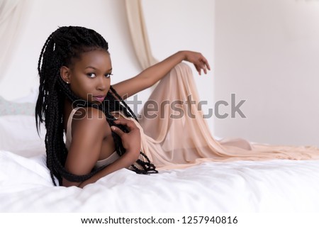 Beautiful African woman with long braids relaxing on her bed in the morning
