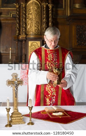 Catholic priest during consecration in a medieval church with 17th century interior Catholic priest during consecration in a medieval church with 17th century interior