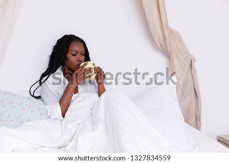 Beautiful African woman with long braids relaxing on her bed in the morning