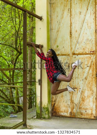 Young black woman during fitness hanging on a rusty old industrial frame