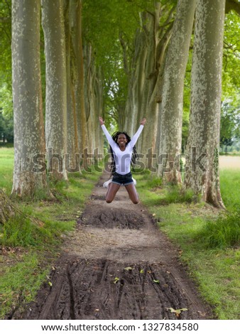 Pretty young African woman with black braids doing big jumps in the park