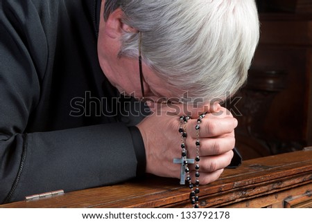 Humble priest kneeling down and praying with his rosary