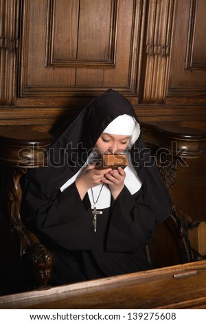 Young nun kissing an old prayer book after praying (shot in a 17th century church interior)