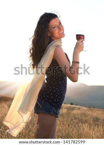 Beautiful happy woman drinking wine during the golden evening hour
