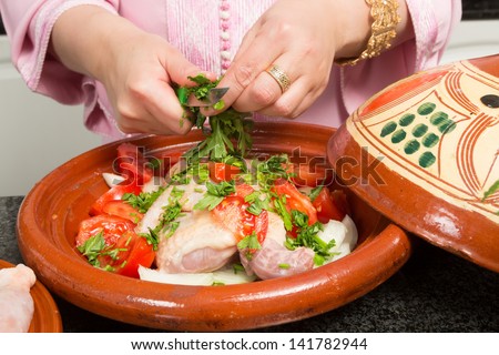 Hands of a woman cutting herbs into a traditional Moroccan tajine during Ramadan nights (Moroccan immigrant woman in modern European kitchen)