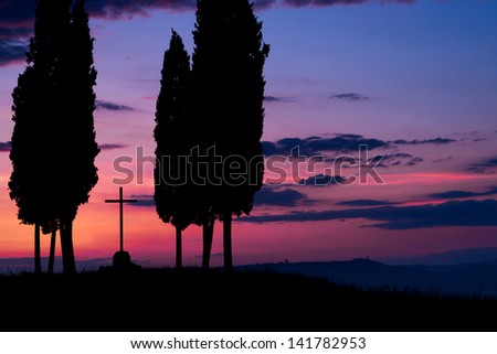Cypress trees and crucifix in darkness just before dawn in Tuscany