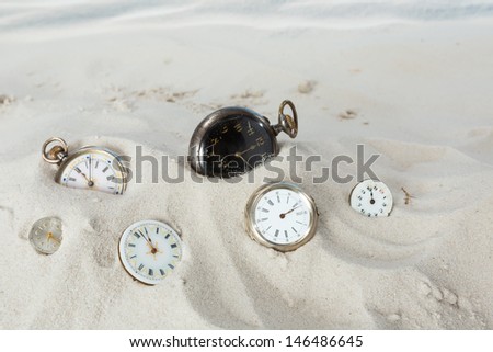 Several antique pocket watches and clocks lying in the beach sand