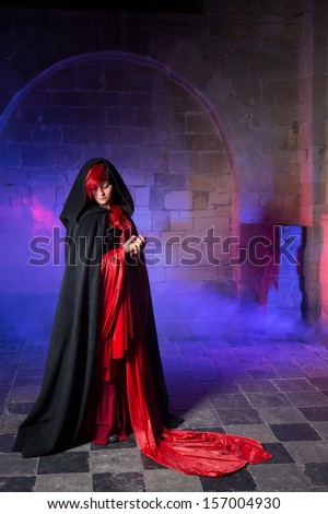 Beautiful gothic victorian woman in red standing in a smokey dark medieval castle