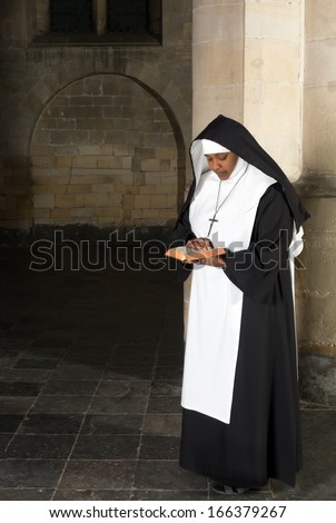 Nun in habit reading the bible in a medieval church