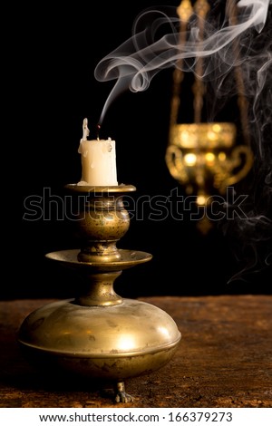 Blown out candle in antique candle stick and in the background a blurred incense thurible