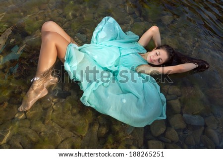 Beautiful woman in green dress floating in the shallow beach waters