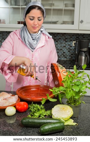 Traditional Moroccan immigrant woman in Europe adding olive oil to her tajine during Ramadan in her modern kitchen