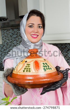 Happy Moroccan immigrant woman in Europe presenting her tajine dish during Ramadan in her modern kitchen
