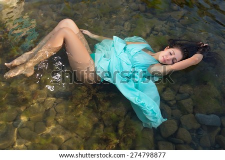 Beautiful woman in green dress floating in the shallow beach waters
