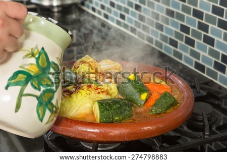 Hands of a woman adding water to a traditional Moroccan tajine during Ramadan nights (Moroccan immigrant woman in modern European kitchen)