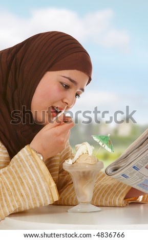 Young veiled woman reading a newspaper and eating ice cream (no brand names can be read)