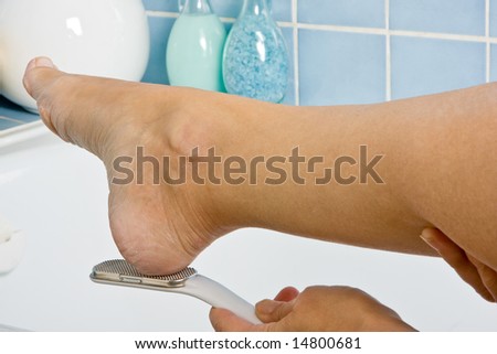 Female hands removing callus from dry feet
