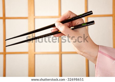 Hands in kimono sleeve holding chopsticks in front of a japanese shoji sliding window