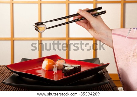 Hands holding sushi with chopsticks in front of a japanese shoji sliding window