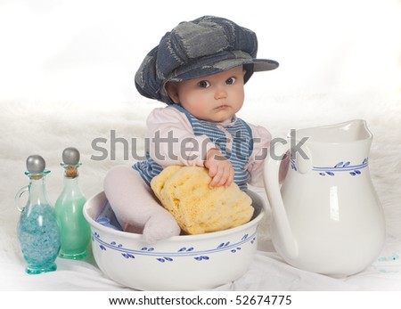 Four months old baby with cap in a wash basin with sponge