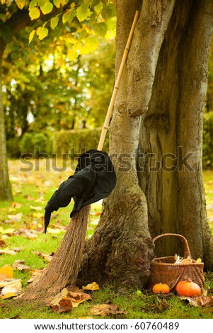 Halloween scene of a witch hat, broom and pumpkin basket against a hollow autumn tree