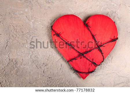 Barbed wire wound around a red heart on a grungy background